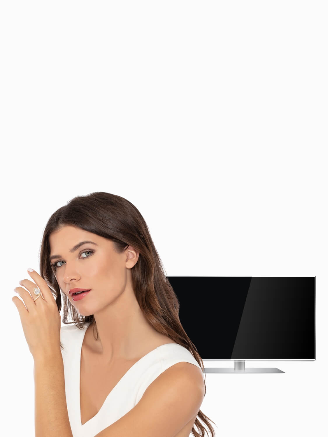 Woman in a white dress wearing diamond ring standing next to a television on a white background