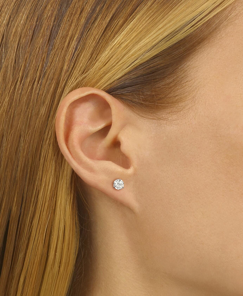 Close-up of an ear wearing a diamond stud earring with blonde hair.