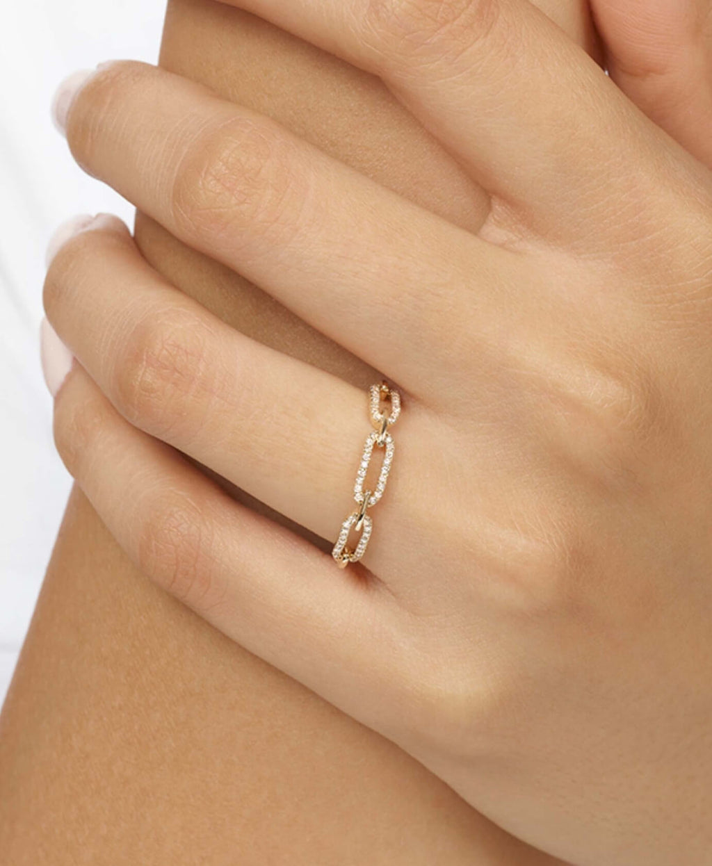 Hand wearing a delicate chain ring on a plain background
