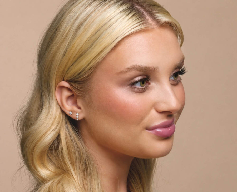 Woman wearing diamond earrings with beige background.
